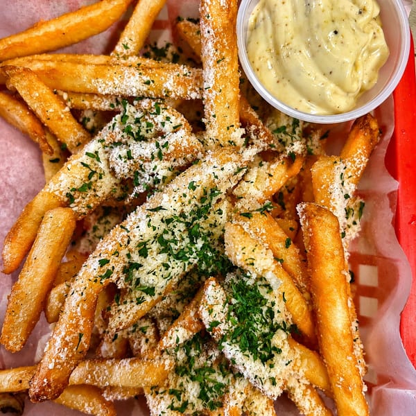 Golden french fries topped with parmesan cheese and parsley, served with a side of creamy dipping sauce.