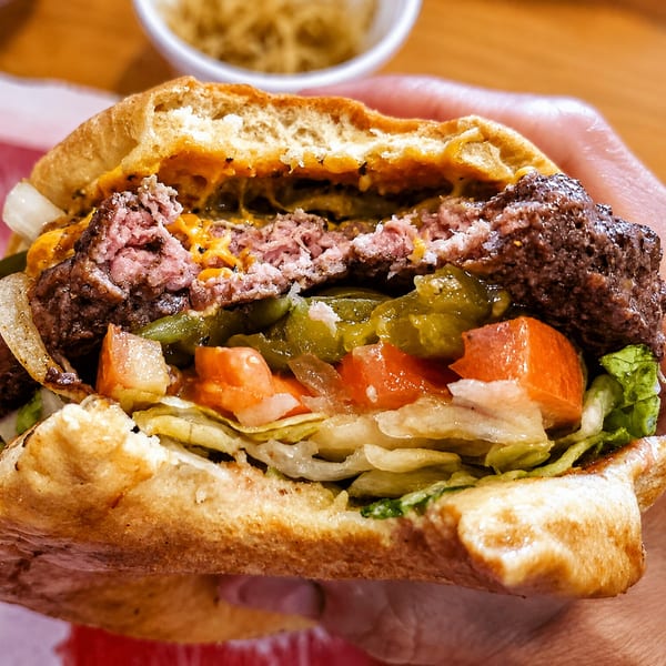 Close-up of a juicy burger, cut in half, revealing melted cheese, meat, lettuce, and tomatoes.