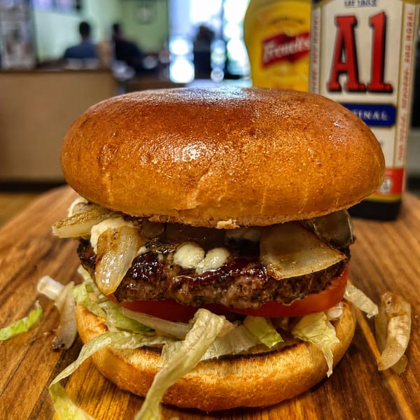 Gourmet burger with melted cheese, caramelized onions, lettuce, and tomato on a wooden board.
