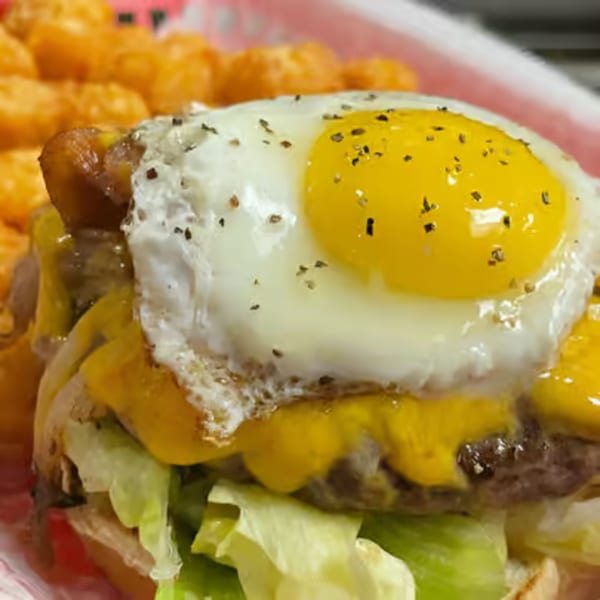 A close-up of a burger with melted cheese, lettuce, and a fried egg, served with tater tots.