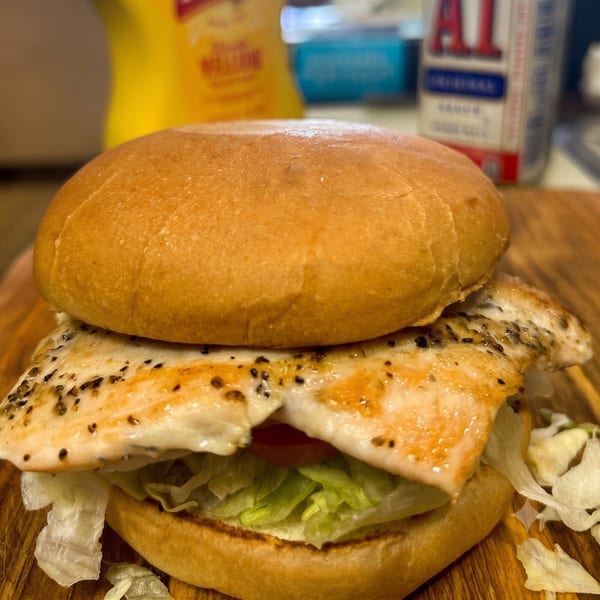 Grilled chicken sandwich with lettuce and tomato on a bun, with condiments in the background.